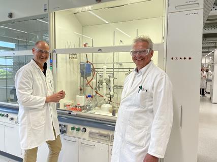 The founders of SBMatrices in a white lab coats standing and smiling before a fumehood
